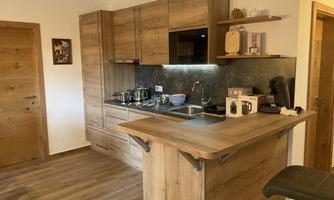 A modern kitchen with wooden cabinets and a spacious dining counter. The equipment includes a stove, sink, and coffee machine.