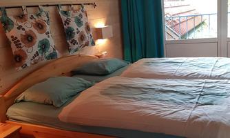 A cozy bedroom with a wooden bed and blue pillows. Turquoise curtains hang in front of the window and there is soft lighting.