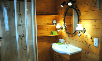 A cozy bathroom with wood-paneled walls. It features a shower, a sink, and warm lighting.