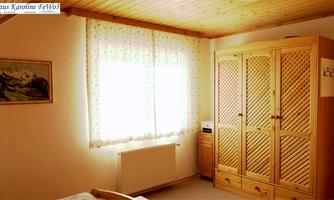 A cozy room with a wooden ceiling and a large wardrobe. The window has soft curtains that let in plenty of light.