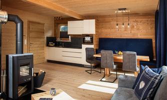 A modern living room with wooden paneling, a dining area, and an open kitchen. In the corner stands a fireplace for coziness.
