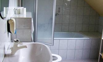 A simple bathroom with a bathtub, a shower, and a sink. The walls are light, and the tiles are kept neutral.