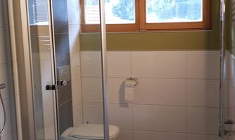 A modern bathroom with a shower and a toilet. The walls are designed in soft colors, and there are large windows letting in daylight.