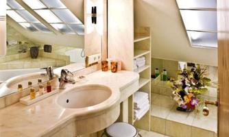 A modern bathroom with an elegant sink and bright tiles. There is a small stool and decorative flowers in the room.