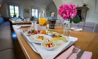 A stylishly set table with our castle breakfast. There are fresh fruits, yogurt, regional culinary products, and a glass of juice, framed by an inviting atmosphere.