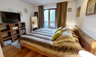 A cozy furnished bedroom with a large bed and a television. The room has wooden flooring and large windows with direct access to the terrace.