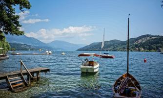 A beautiful lake with boats and gentle hills in the background. The sky is clear and blue, ideal for a relaxing day by the water.