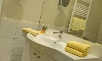 A modern bathroom with a white sink and fresh, yellow towels. The room has bright tiles and a pleasant atmosphere.