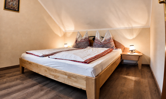 A cozy bedroom with a large bed and two nightstands. The walls are in light colors, a wardrobe, and a seating area.
