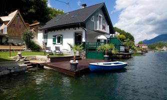 An idyllic house by the water with a small boat and green surroundings. The clouds in the blue sky give the scene a relaxed atmosphere.