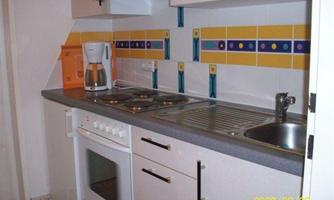 A modern kitchen with a stove, a sink, and a kettle. The walls are bright and decorated with colorful tiles.