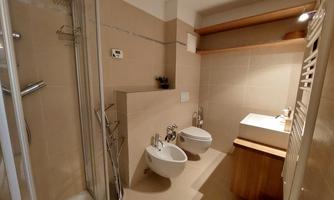 A modern bathroom with a shower, sink, and two toilets. The walls are in neutral colors and there are wooden shelves.