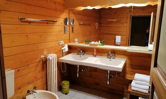 A cozy bathroom with wooden paneling. There are two sinks, a toilet, and fresh towels.