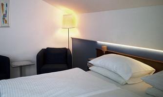 A modernly furnished bedroom with a large bed and comfortable armchair. Soft lighting creates a pleasant atmosphere.