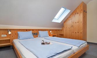 A cozy bedroom with wooden walls and two single beds. The skylight ensures daylight and a friendly atmosphere.