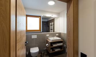 A modern bathroom with a white toilet and a sink on a wooden shelf. There is a window that lets in natural light.