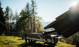 A beautiful view of a green meadow with a wooden bench and sunshade. In the background, trees and mountains can be seen.