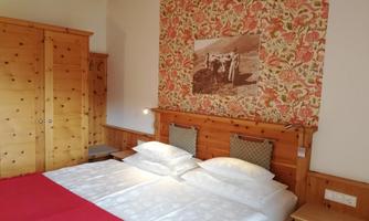 A cozy bedroom with a double bed and wooden paneling. On the wall is a floral pattern and an old photo decorated.