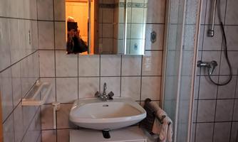 A bathroom with a shower cubicle, sink, and a mirror. The walls are tiled and the ceiling is made of wood.
