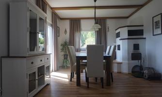 An elegant dining area with a large table and white chairs. The room is bright and cozy, with a fireplace and large windows.