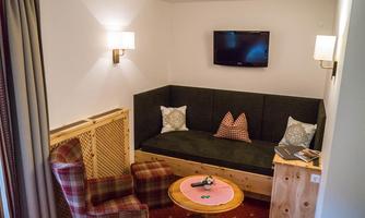 A cozy living room with a comfortable seating area and a television on the wall. There is also a round table and an armchair with a checkered pattern.