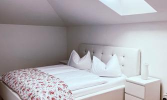 A cozy bedroom with a white bed and a floral patterned duvet. Above the bed, there is a skylight that provides plenty of daylight.