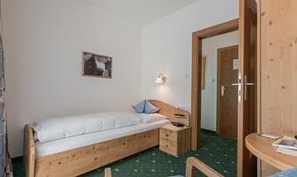A simple room with a bed and a chair. The walls are light and the floor is covered with green carpet.