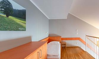A simple room with wooden flooring and a bed. On the wall hangs a picture of a green landscape.