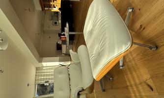 A stylish armchair with a matching footrest is in a modern room. The floor is made of wood and the light is bright and inviting.