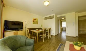 A modern living room with a cozy armchair and a dining table. A television and a light source complement the space.