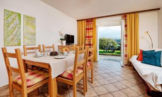 A cozy living space with a dining area and a view of the outdoors. Plenty of light pours in through the large windows, and the decor is bright and inviting.