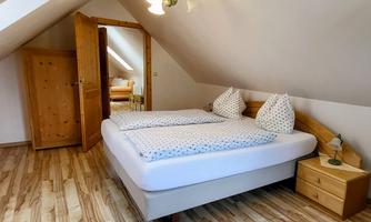 A cozy bedroom with a double bed and two pillows. The room has a wooden floor and a sloped ceiling.