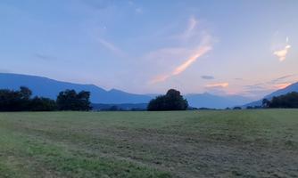 A spacious meadow with hills in the background. The sky is blue with gentle clouds and a soft sunset.
