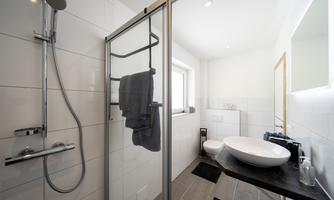 A modern bathroom with a shower, sink, and high-quality fittings. The walls are brightly tiled and there are large windows for plenty of daylight.