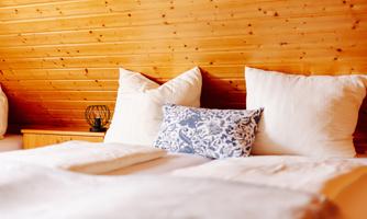 A cozy bedroom with wood paneling and large pillows. A decorative blue pillowcase lies on the bed.