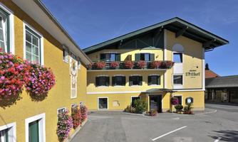 A charming hotel with a yellow facade and blooming flower boxes. The clear sky and well-maintained surroundings create an inviting atmosphere.