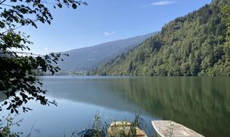 A quiet lake surrounded by green hills and trees. In the foreground, boats are placed on the shore.