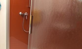 A modern shower with a turquoise wall and an orange back wall. The showerhead and the faucet are made of stainless steel.