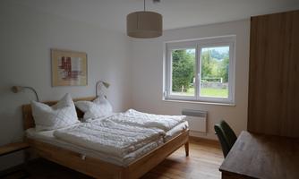 A bright bedroom with a double bed and two pillows. The room has a window with a view of the greenery and modern furniture.