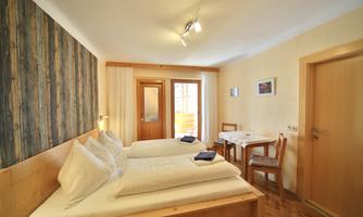 A cozy room with two beds and a small dining area. There is plenty of daylight in front of the window and a warm color scheme.