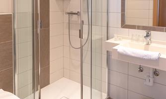 A modern bathroom with a glass shower and a sink. The walls are brightly tiled and the floor is made of wood.