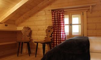A cozy wooden house with a wooden ceiling. Two chairs and a window with red-checked curtains create a warm atmosphere.