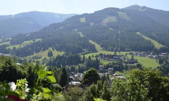 A picturesque landscape with green mountains and meadows. In the foreground, small houses and trees can be seen.