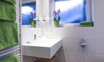 A modern bathroom with a white sink and a large mirror. A green towel and a small plant create a fresh atmosphere.