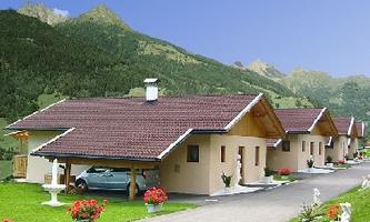 A quiet residential area with modern houses and blooming flower beds. In the background, green mountains can be seen.