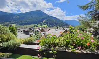 A beautiful view of the mountains with green meadows and pretty flowers on a balcony. The sky is clear and sunny.
