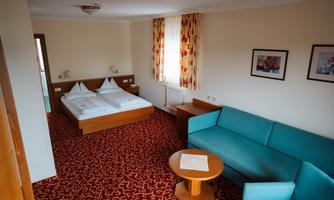 A cozy hotel room with a double bed and a blue sofa. There is a table and colorful curtains at the windows.