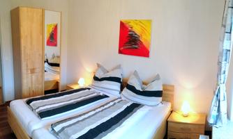 A cozy bedroom with a double bed and stylish cushions. The walls are light, and a colorful piece of artwork gives the room character.