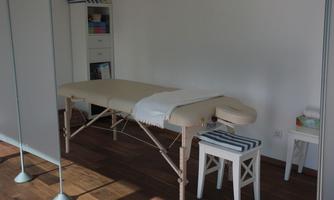 A quiet massage area with a treatment table and a small seating area. The walls are bright, and the room is well lit.
