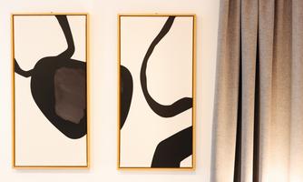 Two abstract paintings in golden frames hang on the wall. The artworks feature black shapes on a white background.